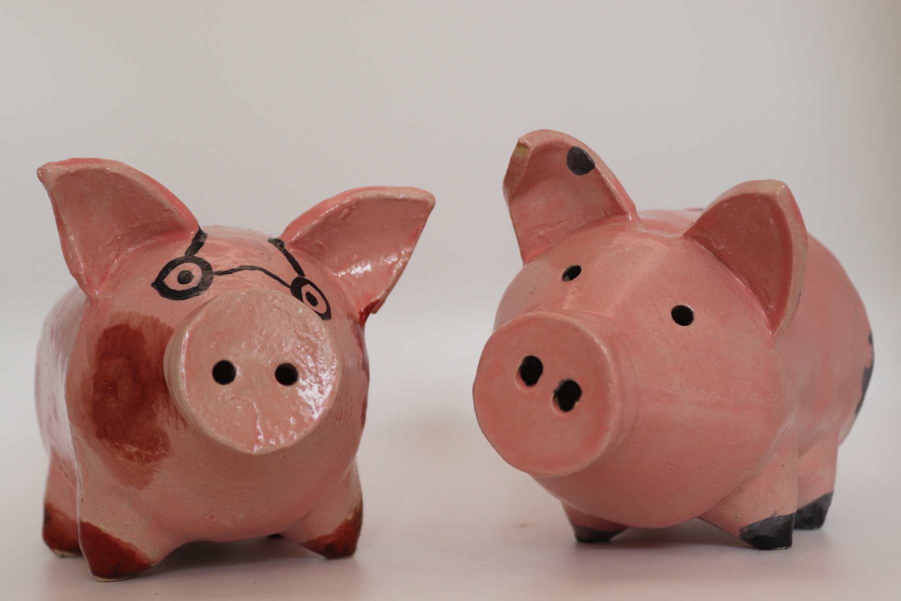 Two pink ceramic piggy-bank tests, one with painted glasses