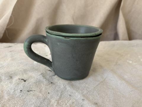 Small handmade green stoneware mug on a cloth-covered table